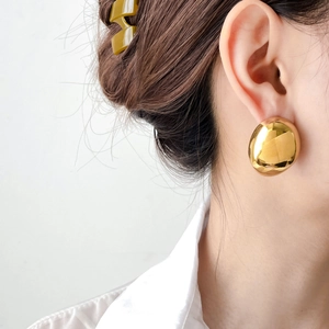 Detailed close-up of large polished gold hollow teardrop earrings on a model with shirt