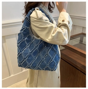 Detail of blue denim shoulder bag featuring quilted diamond pattern and fringe texture
