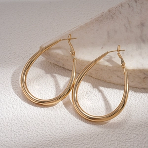 Polished gold drop hoop earrings leaning on white textured stone background