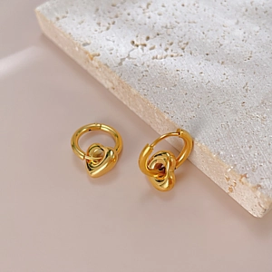 Boucles d'oreilles cœur dorées polies sur décor pierre avec fond rose chaud
