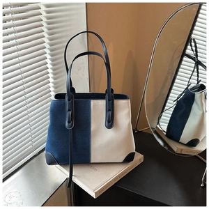 Detail of the blue and white denim tote bag showing leather handles in a chic studio setting