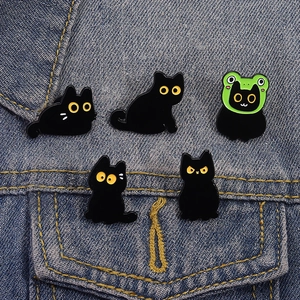 Close-up of five cute black cat enamel pins styled on a blue denim jacket pocket