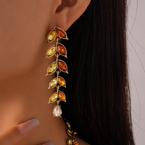 Macro shot of long leaf-shaped earrings with amber gradient stones and a crystal drop