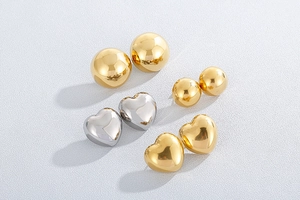 Polished heart and sphere earrings in gold and silver finish on white background