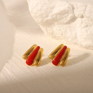 Macro shot of 18k gold-plated earrings with red enamel detail on stone background