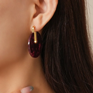 Close-up of model wearing round dark red acetate earrings with golden metal accents