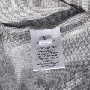 Detailed laundry label on gray knitted fabric showing size S and 100% polyester material