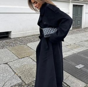 Détail du long manteau noir en laine avec sac à chaîne matelassé dans une rue de la ville