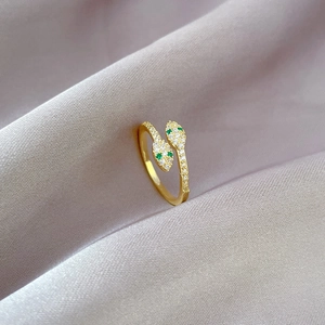 Adjustable gold snake ring featuring green eyes and white cubic zirconia on purple silk