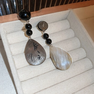 Detail of asymmetric shell teardrop earrings with black bamboo pattern and beads