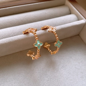 Detailed shot of gold C-shaped earrings with teal enamel four-leaf clover design