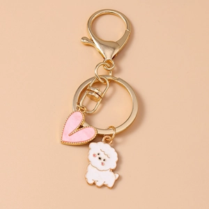 Detail view of a golden metal keychain with pink enamel heart and a curly white puppy dog