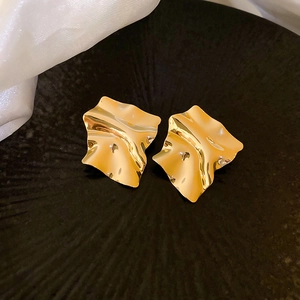 Macro shot of irregular pleated square gold earrings on a textured black background