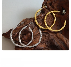 Close-up of gold and silver bamboo joint C-shape earrings on a natural wood block