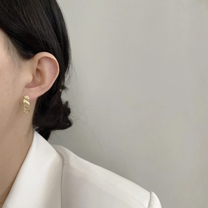 Detail shot of hammered gold-tone textured earrings worn with a white blazer