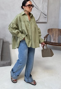 Detail view of stylish sage green pleated oversized shirt and light blue wide-leg jeans