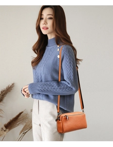 Close-up of a brown leather crossbody bag styled with a blue sweater on a female model
