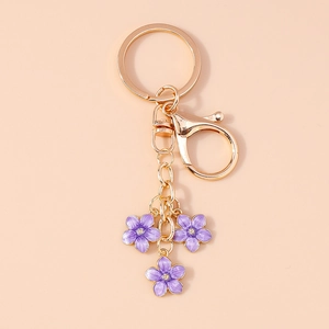 Detail of three purple enamel flower pendants on a gold-plated metal keychain with lobster clasp