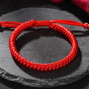 Handcrafted red woven bracelet with traditional Vajra knot on black rock surface