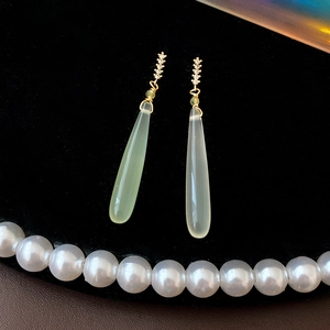 Close-up of teardrop earrings with green stones and gold accents on black velvet background