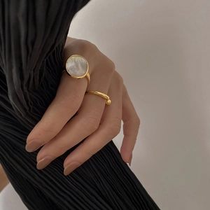 Close-up of stacked gold rings with a large round white mother of pearl inlay on hand