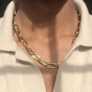 Macro detail of golden paperclip chain necklace worn over a white knitted shirt collar