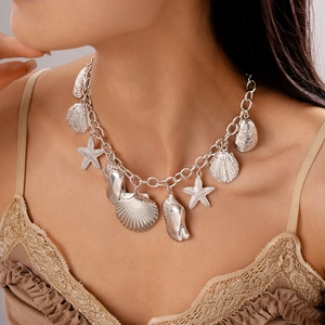 Close-up of a silver starfish and seashell charm necklace on a model's neck