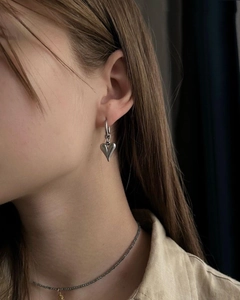 Primo piano di un orecchino pendente a forma di cuore d'argento indossato da una modella