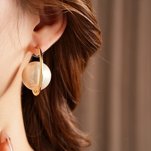 Close-up of a vintage gold C-shape hoop earring featuring a large pearl on a female model