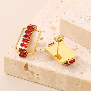 Macro view of rectangular gold earrings with red zircons and white mother-of-pearl