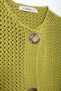 Macro shot of green hollow knit vest featuring a round neck and gold metal button detail