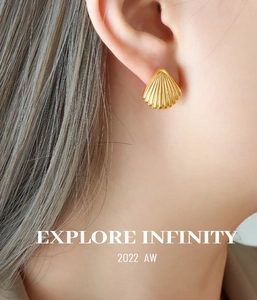 Detail of gold shell-shaped earrings with radial stripes on a model's ear