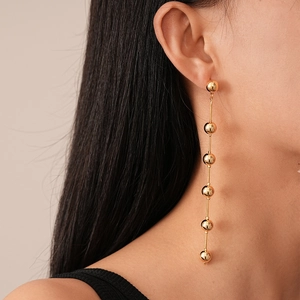 Close-up of long gold beaded tassel earring with six polished metal spheres on earlobe