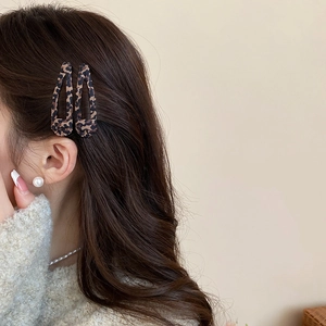 Dettaglio di fermagli per capelli leopardati su capelli castani mossi e accessori di perle