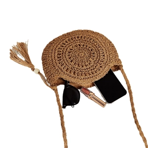 Round straw crossbody bag in natural brown with tassel and daily essentials inside