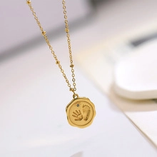 Close-up of golden necklace with baby handprint and footprint engraved on round pendant