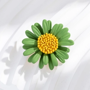 Macro view of green daisy brooch with textured yellow center on wavy white backdrop