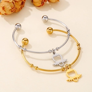 Detail of gold and silver titanium steel open bangles with angel wing heart charms