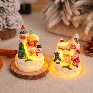 Close-up of lighted miniature resin Christmas house and snowman with warm LED glow