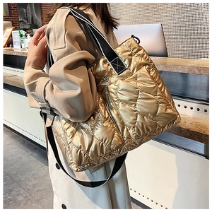 Close-up of golden quilted puffer tote bag with glossy finish on model shoulder