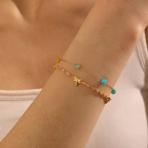 Detail of layered gold dragonfly bracelet with colorful beads on a model's wrist