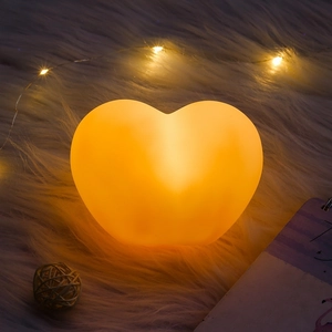 Close-up of heart-shaped night light with warm orange glow on white plush rug