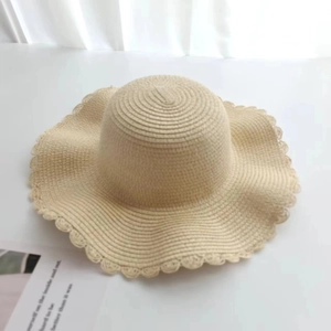 Detail of beige straw hat featuring fine weave texture and scalloped wavy edge design