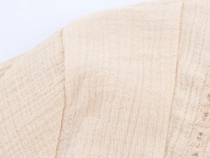 Detail of beige seersucker fabric with intricate embroidery and pleated texture