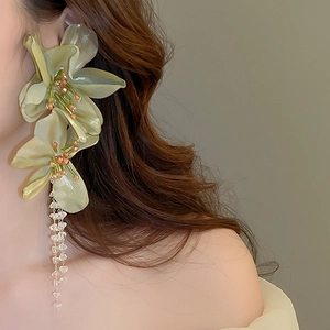 Close-up of oversized light green lace flower earrings with champagne bead tassels on a model