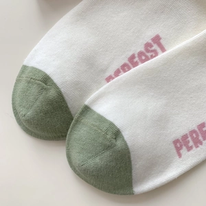 Close-up of white knitted cotton sock with green toe and pink PERFECT lettering detail