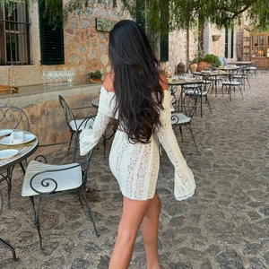 Back view of a white lace off-shoulder long-sleeve mini dress in a garden setting