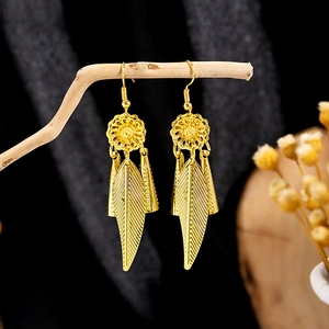 Detail of golden bohemian peacock earrings with floral hollow design and textured leaf pendants