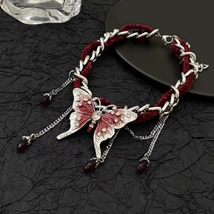 Détail du choker en velours rouge avec pendentif papillon, chaînes argentées et pompons