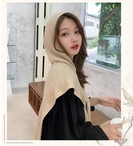 Detailed knit texture of beige hooded scarf wrap on model in soft indoor lighting